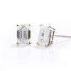 A pair of emerald-cut diamond stud earrings in a silver four-prong setting, shown on a clean white reflective surface.