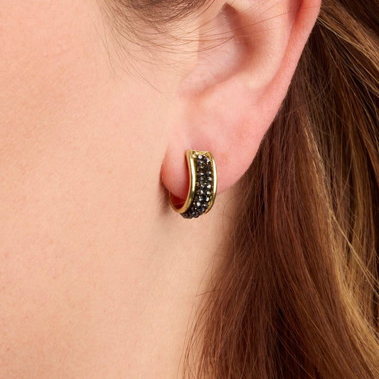Small black diamond hoop earrings in gold displayed on a model's ear.